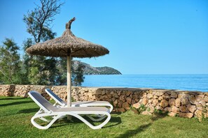 Una silla de descanso blanca con sombrilla de paja, un muro de piedra y vista al mar y una isla distante.