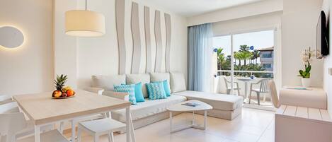 A modern living room with a sofa, a dining table, and chairs. There is a large window with a view of palm trees and buildings.