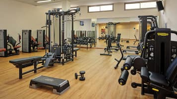 Een sportschool met diverse fitnessapparaten, waaronder krachttoestellen, losse gewichten en een bank.