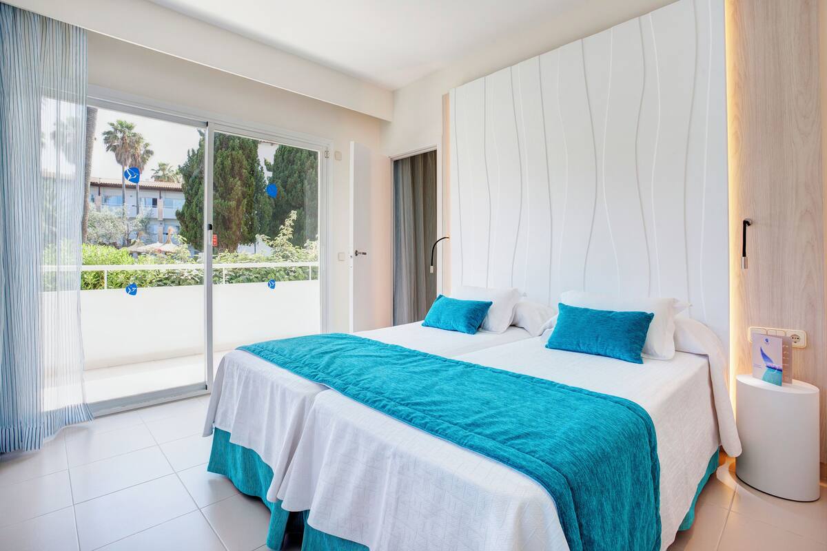 A hotel room with a large bed, a bedside table, and a view of the outdoors.