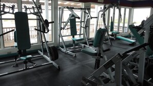 A gym with various exercise machines, benches, and a view of the outdoors through large windows. - Island Resort (Chincoteague)