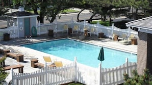 A rectangular swimming pool surrounded by a white picket fence, with lounge chairs and umbrellas. - Island Resort (Chincoteague)
