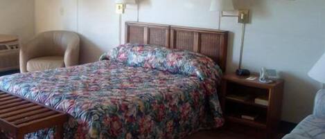 A hotel room with a bed, a chair, a bedside table, and a lamp.