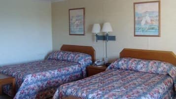 A hotel room with two beds, a nightstand with a lamp, and two framed pictures on the wall.