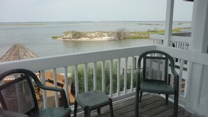 A balcony with two chairs and a view of a calm body of water with a small island. - Island Resort (Chincoteague)