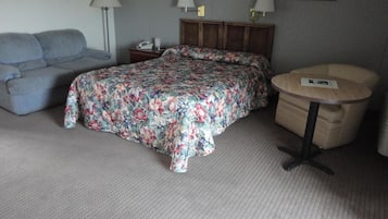 Ein Schlafzimmer mit Bett, einer Couch, einem Nachttisch, einer Lampe und einem kleinen runden Tisch.