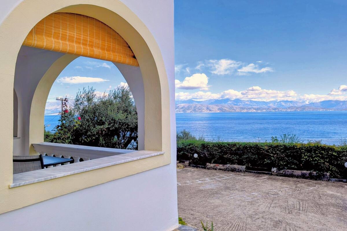 Vista a través de un arco de ventana sobre un paisaje costero con montañas al fondo.