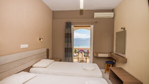 A hotel room with two beds, a desk, a chair, a TV, and a balcony with a view of the sea. - Dionysos Apartments (Corfu)