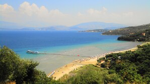 A coastal beach with clear waters, a pier, and a sandy beach area. - Dionysos Apartments (Corfu)