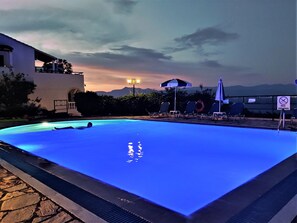 A swimming pool with lounge chairs and a 'No Diving' sign, surrounded by a building and mountains in the background. - Dionysos Apartments (Corfu)