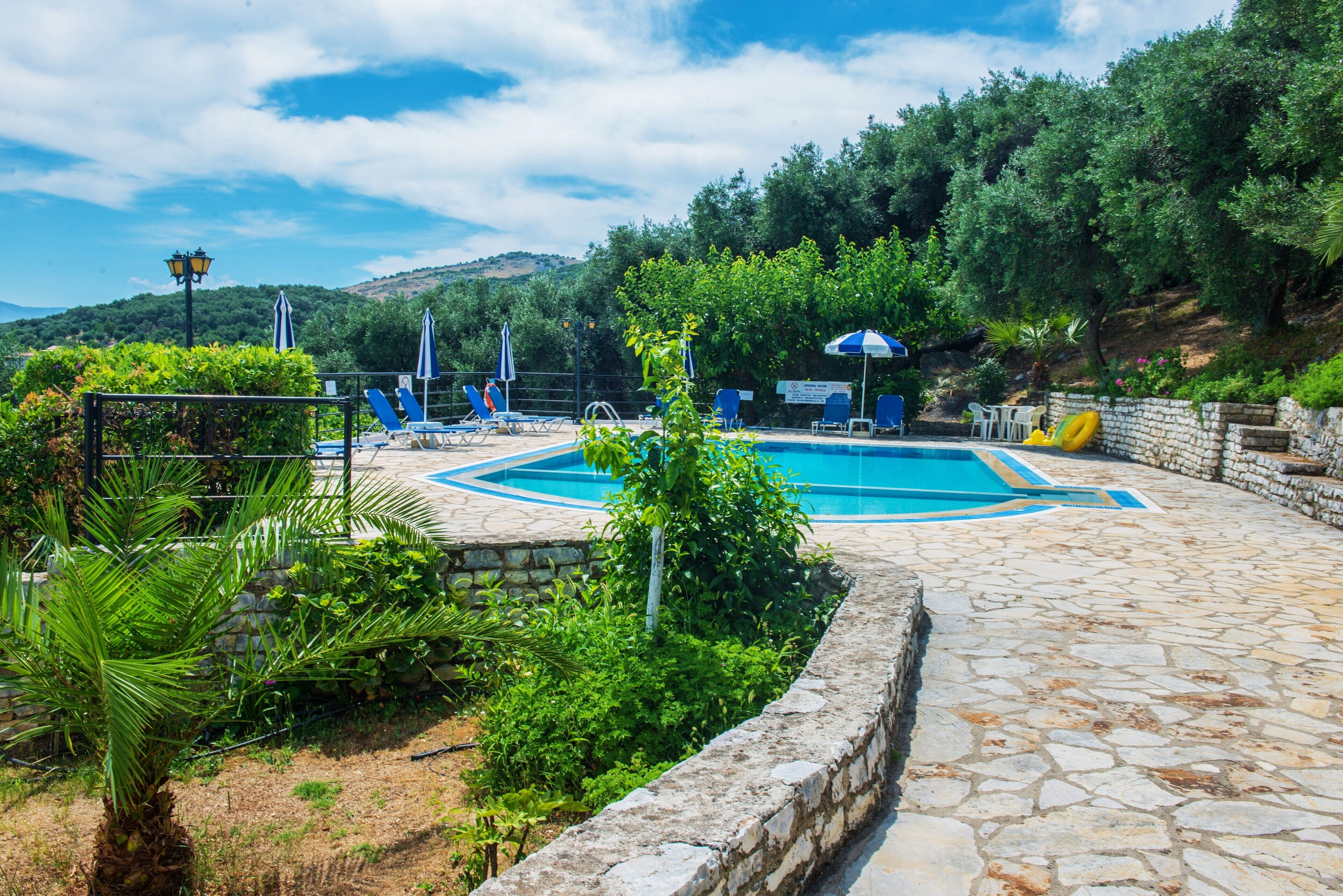 A swimming pool with lounge chairs and umbrellas, surrounded by stone walls and greenery.