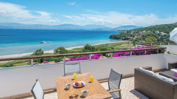 A balcony with a wooden table, chairs, and a view of the sea and mountains. - Dionysos Apartments (Corfu)