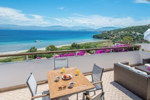 A balcony with a wooden table, chairs, and a view of the sea and mountains. - Dionysos Apartments (Corfu)