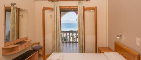 A hotel room with a bed, a wooden nightstand, a bedside table, a mirror, a bathroom mirror, a window with curtains, and an air conditioning unit.