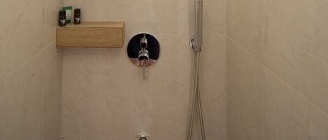 A modern shower with a handheld showerhead, a wall-mounted faucet, and two wooden shelves with toiletries.