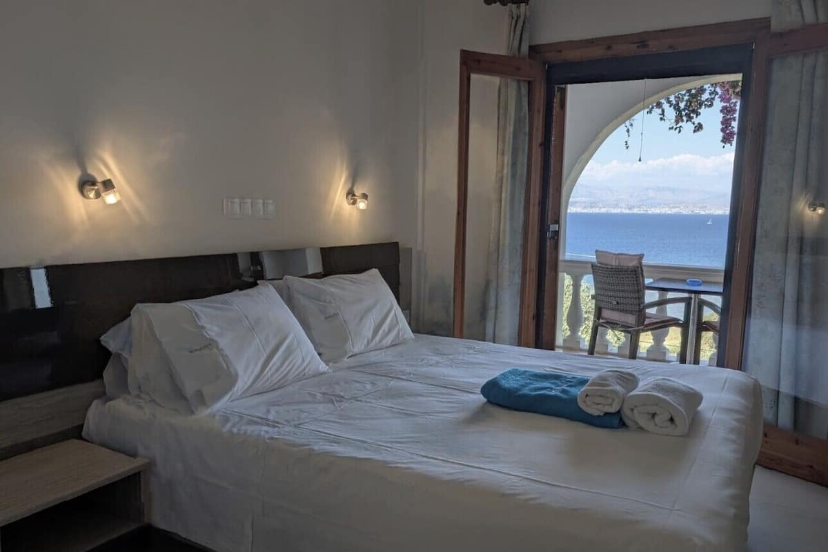 Un dormitorio con cama, mesita de noche y vista al mar a través de un ventanal.