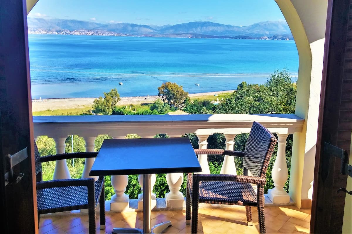 Un balcón con mesa y sillas, con vistas a un paisaje costero con montañas al fondo.