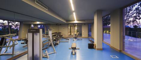 Un gimnasio con equipo de ejercicio, ventanas amplias y suelo azul.