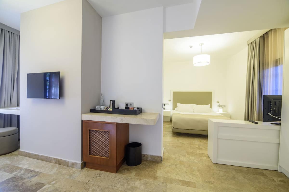 A hotel room with a bed, bedside table, TV, and a small seating area.
