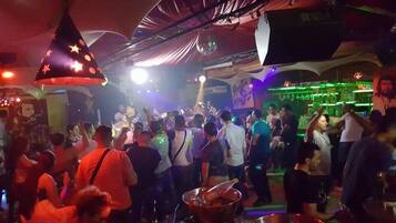 Un bar concurrido donde la gente baila y hay un escenario para música en vivo.