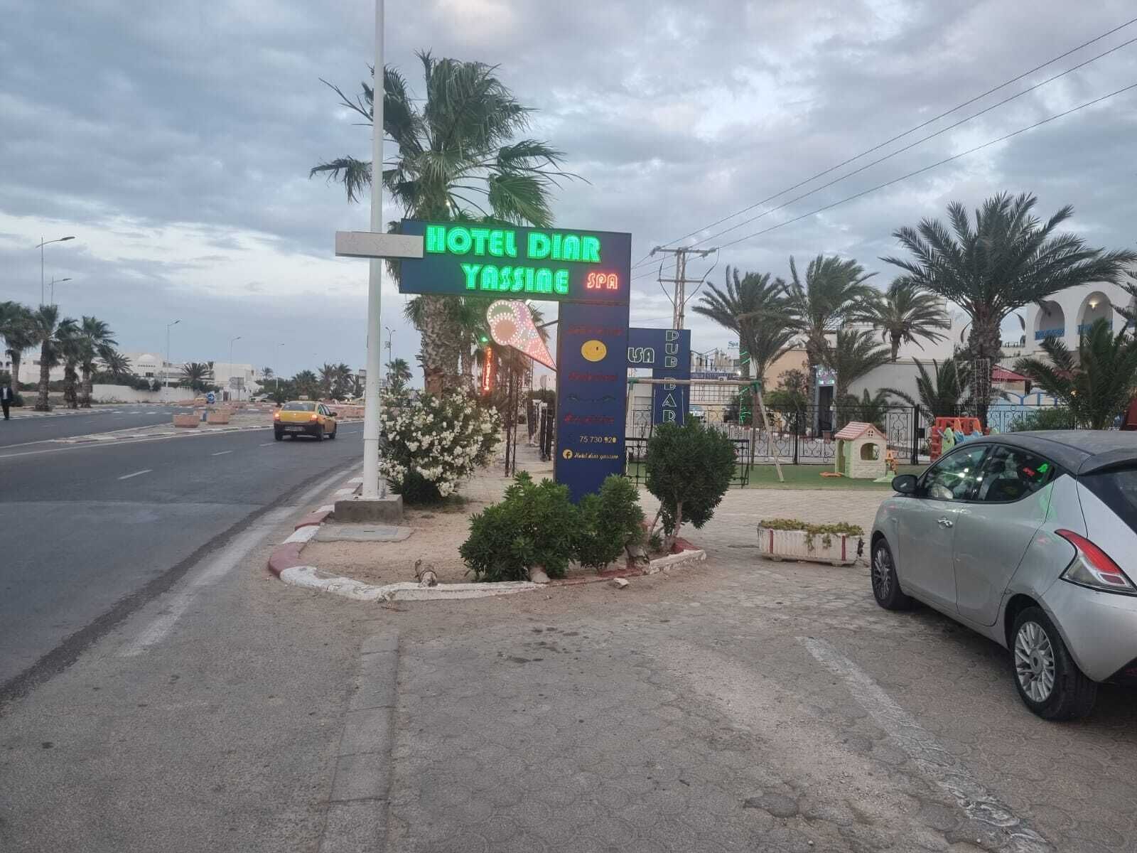 A hotel sign with a neon signboard, palm trees, and a parked car.