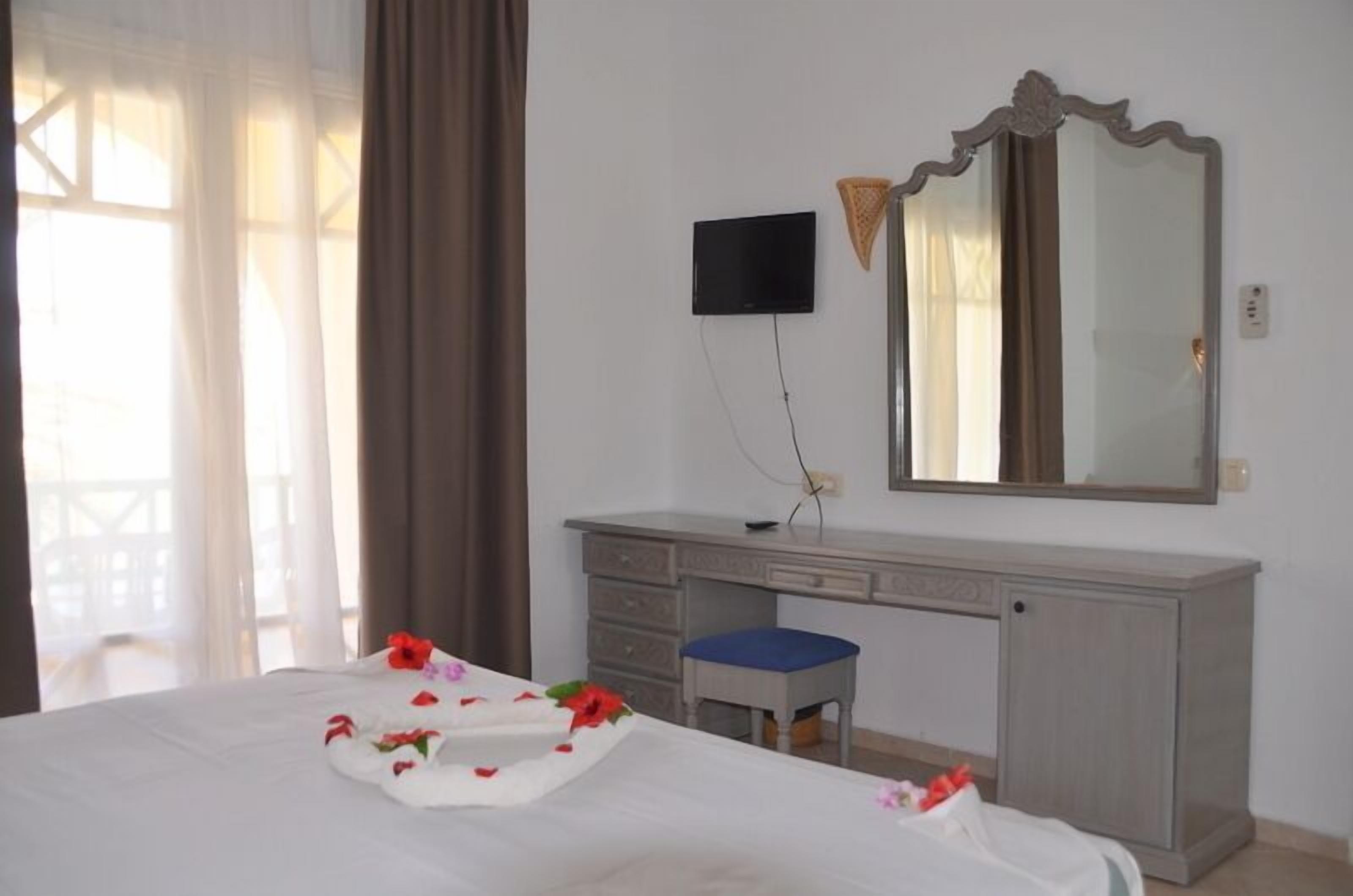 A hotel room with a bed, a desk, a chair, a TV, and a large mirror.
