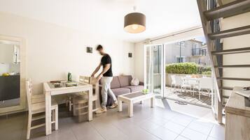 A modern living room with a dining area, a sofa, and a staircase leading to an outdoor patio.