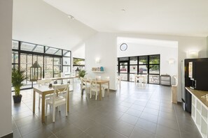A spacious, well-lit room with large windows, a dining area with white furniture, and a kitchen area with a refrigerator and cabinets. - Garden & City Mont Ventoux - Malaucène (Malaucene)