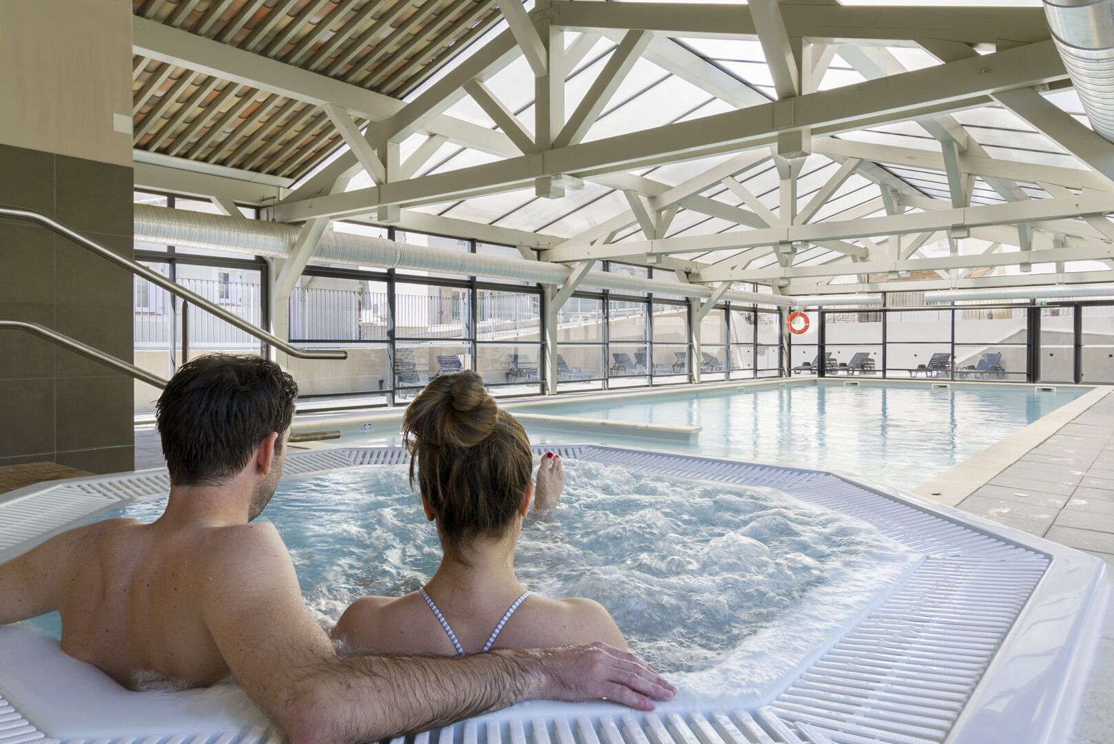 A couple relaxing in a hot tub with a view of the pool area and lounge chairs.