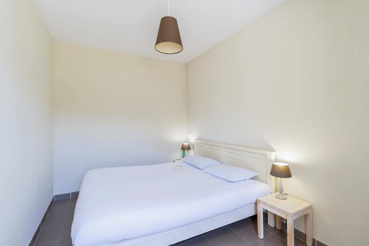 A small, clean bedroom with a single bed, bedside lamps, and a hanging light fixture.