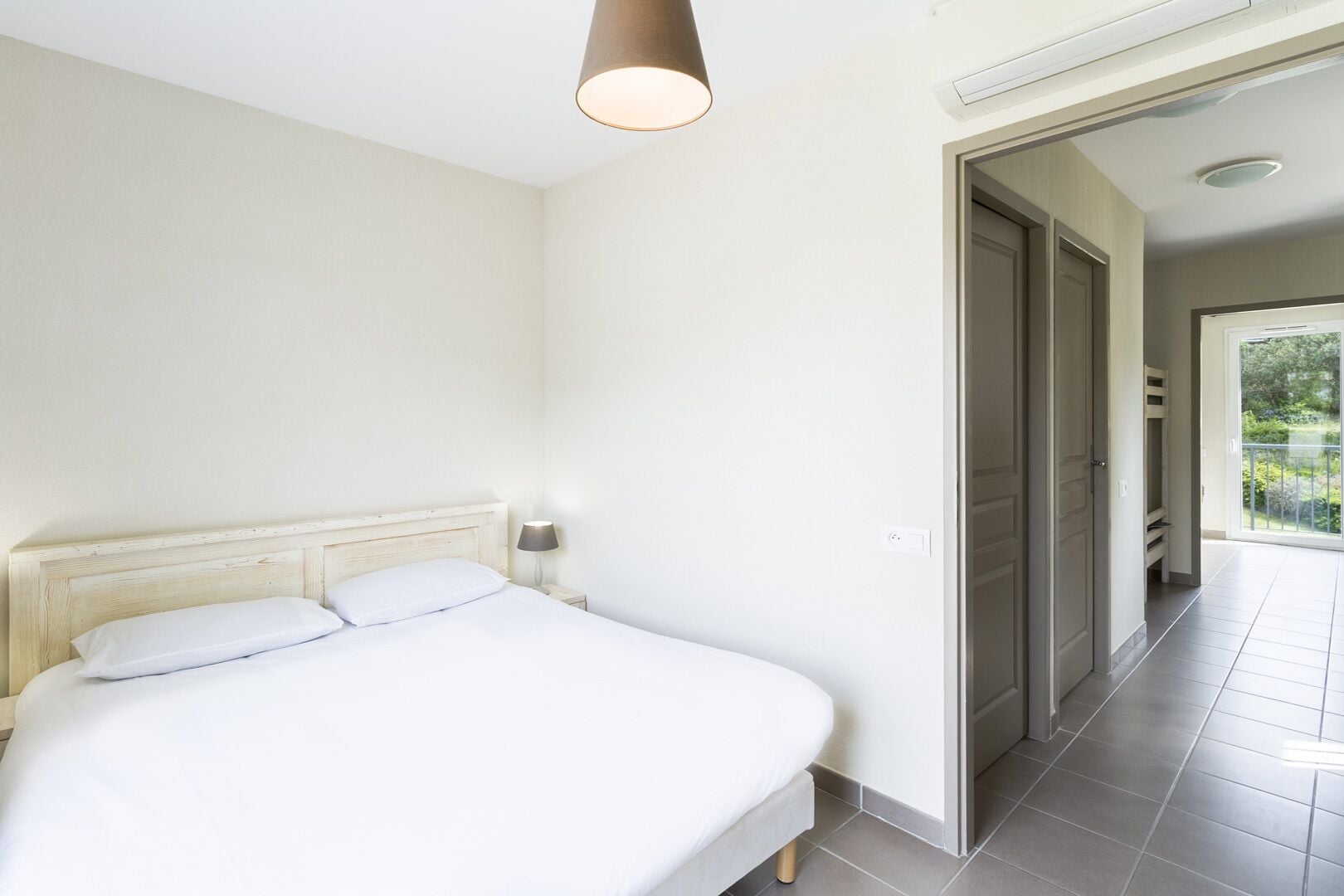 A bedroom with a bed, a nightstand, a lamp, and a door leading to a balcony.