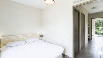 A bedroom with a bed, a nightstand, a lamp, and a door leading to a balcony.