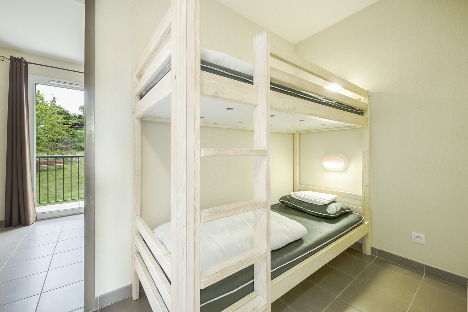 Une chambre avec un lit superposé donnant sur un balcon et une fenêtre.