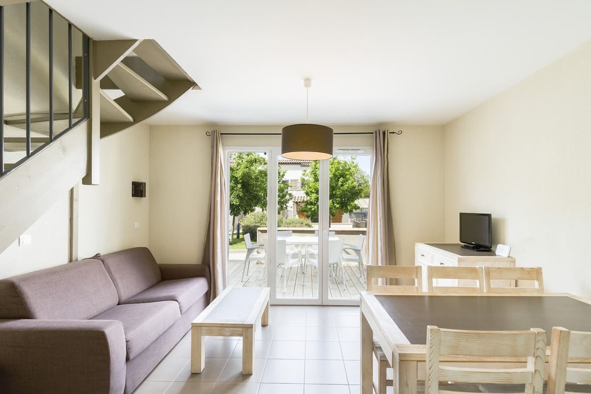 A modern living room with a sofa, a wooden dining table, and a TV.