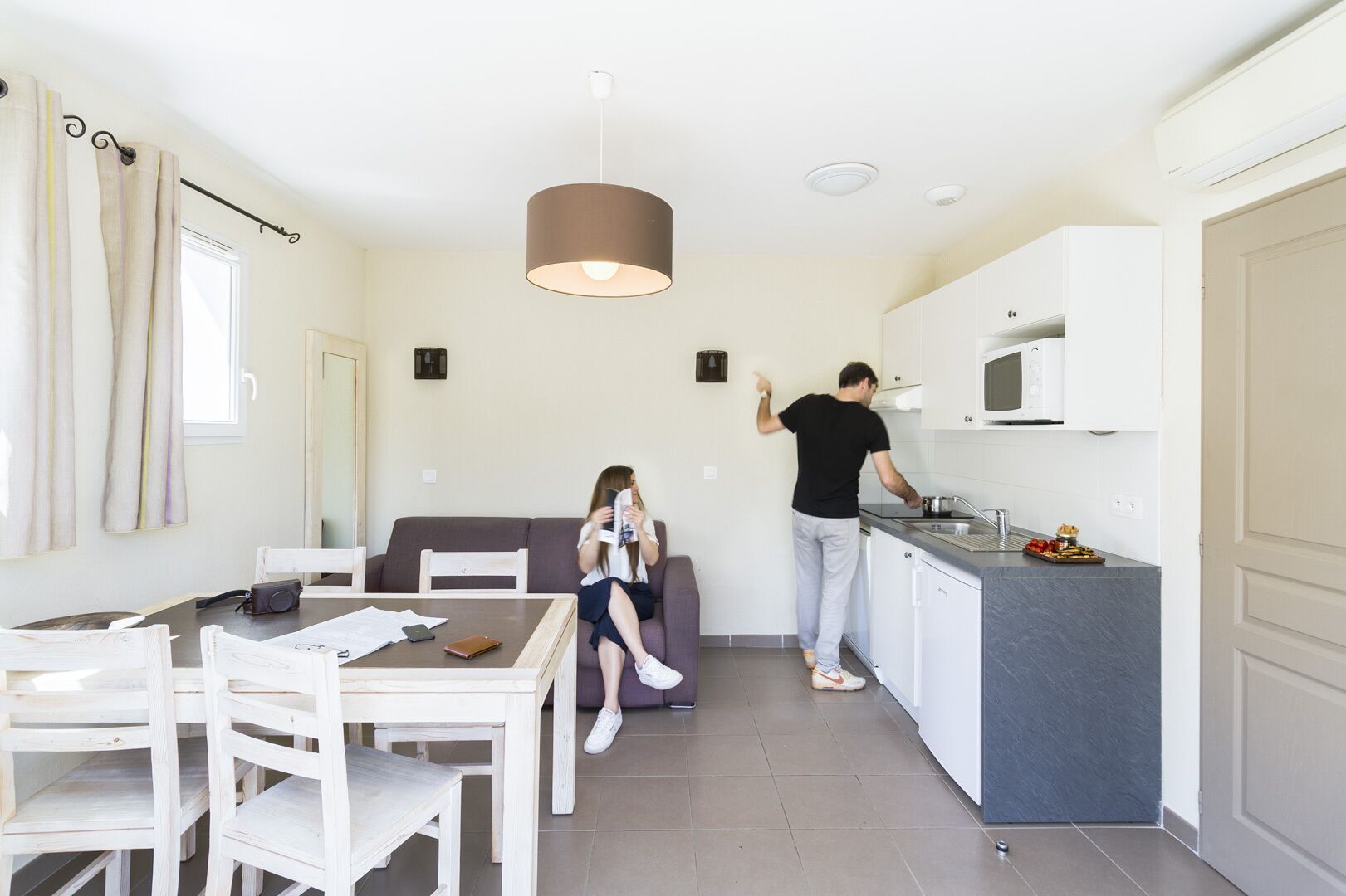 Una cocina moderna con armarios blancos, encimera gris y una lámpara colgante.