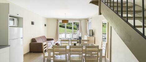 A modern kitchen with a dining area, a sofa, and a staircase leading to an outdoor patio.