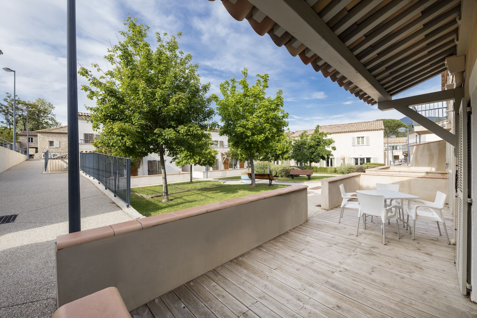 Une terrasse extérieure couverte, dotée d’un plancher en bois, de chaises blanches et d’une petite table.