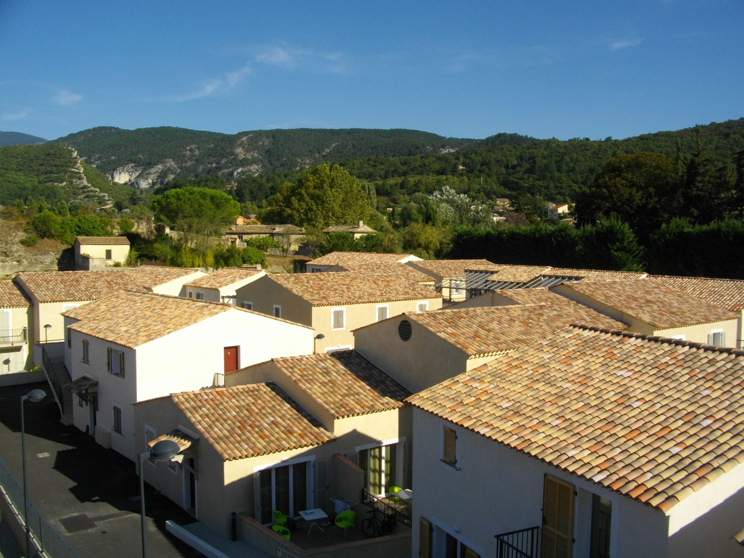 Une rangée de bâtiments blancs aux toits de tuiles rouges, disposés dans un quartier résidentiel, avec une chaîne de montagnes en arrière-plan.