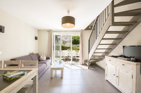 A modern living room with a sofa, coffee table, and TV stand. There is a staircase leading to an upper level.