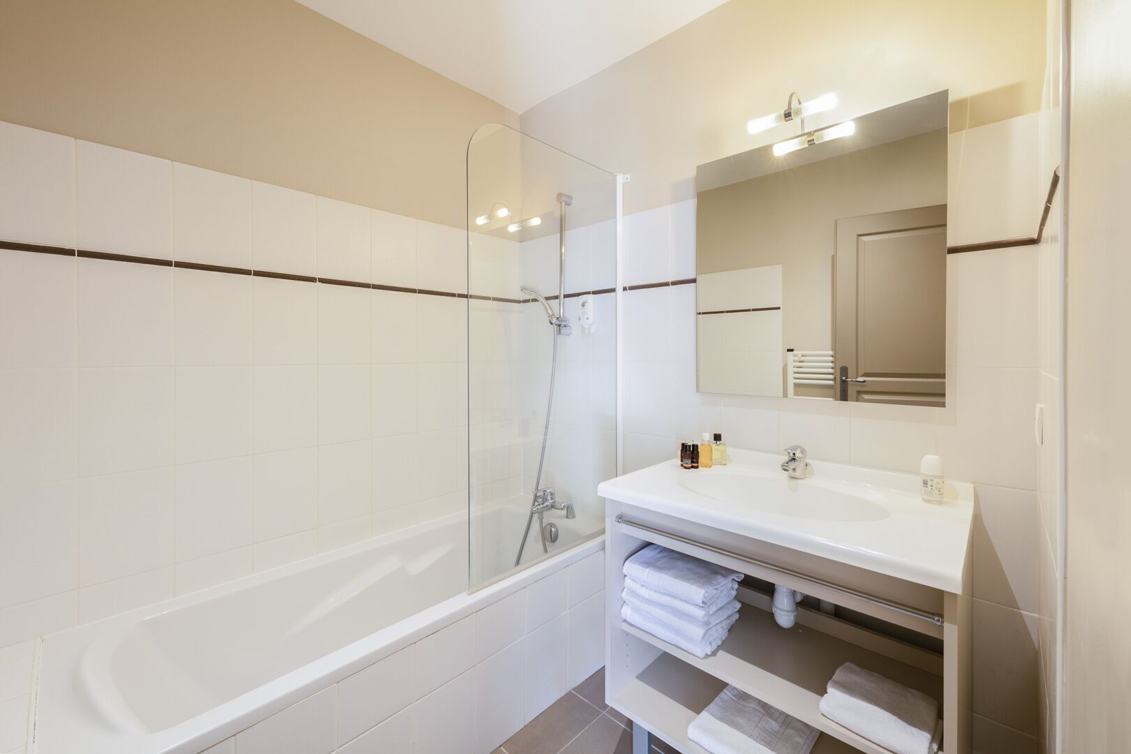 A modern bathroom with a glass-enclosed shower, a white vanity with a mirror, and neatly folded towels.