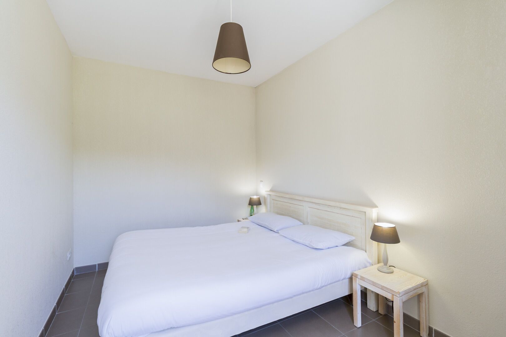 Habitació petita i neta amb un llit individual, una taula de nit i una làmpada penjant.