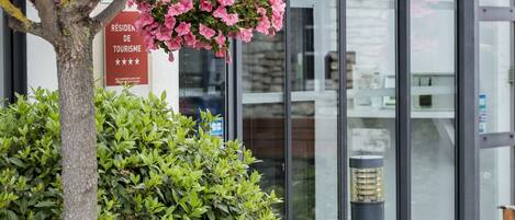 A hotel entrance with a sign indicating it is a residence hotel, a potted plant, and a hanging flower arrangement.