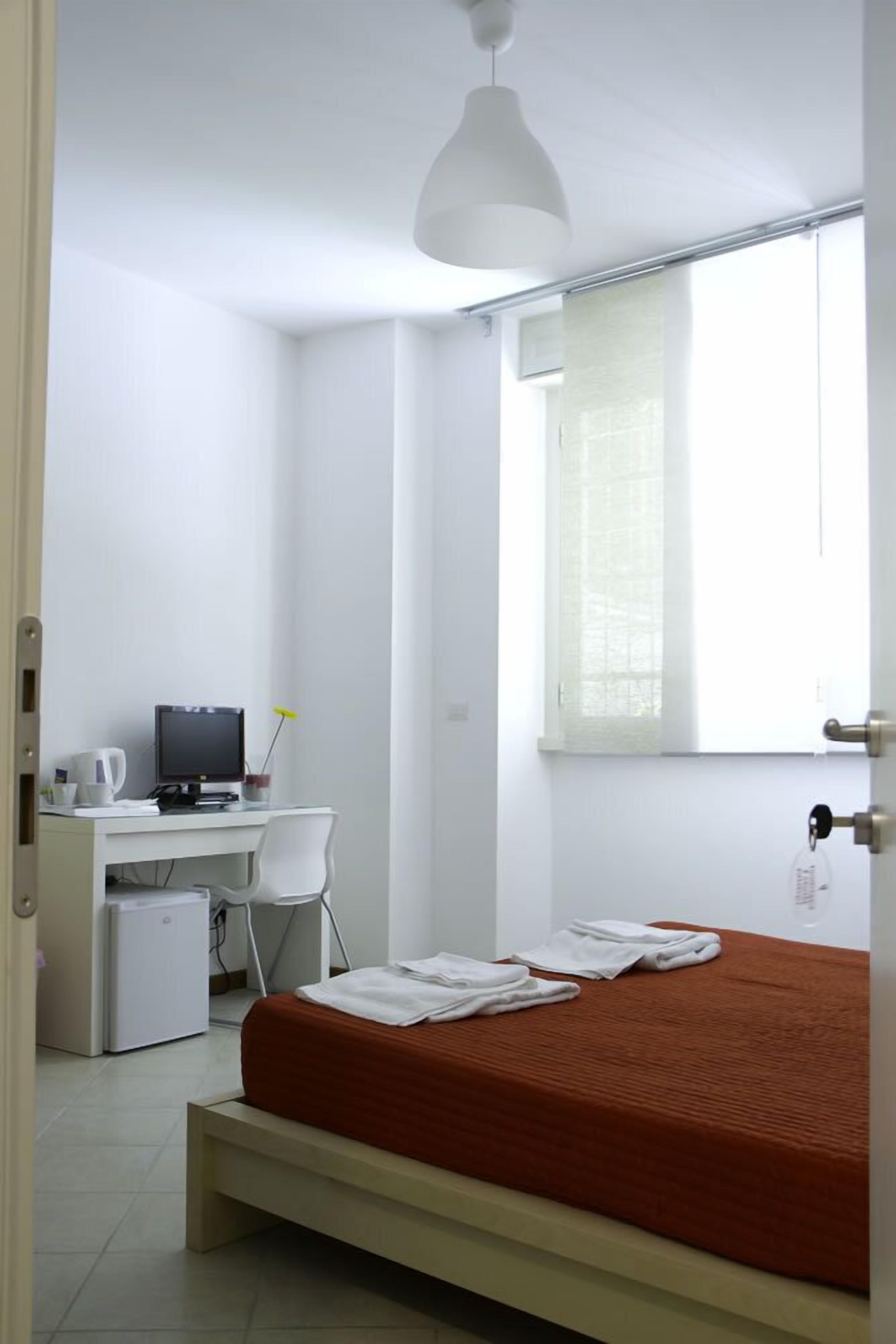 A bedroom with a bed, a desk with a computer, a chair, and a window with blinds.