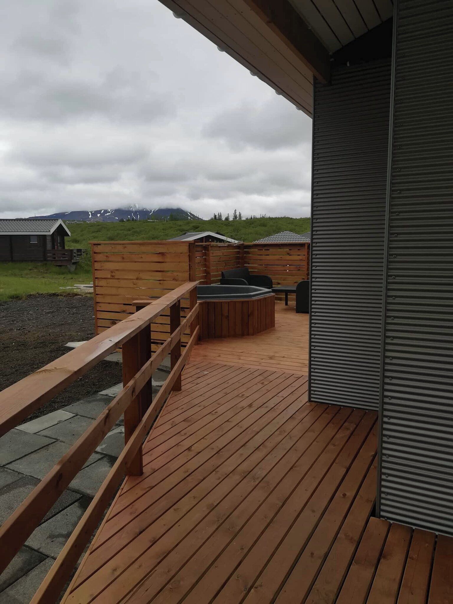 Una terraza de madera con barandilla, zona de estar y vistas a un paisaje montañoso.