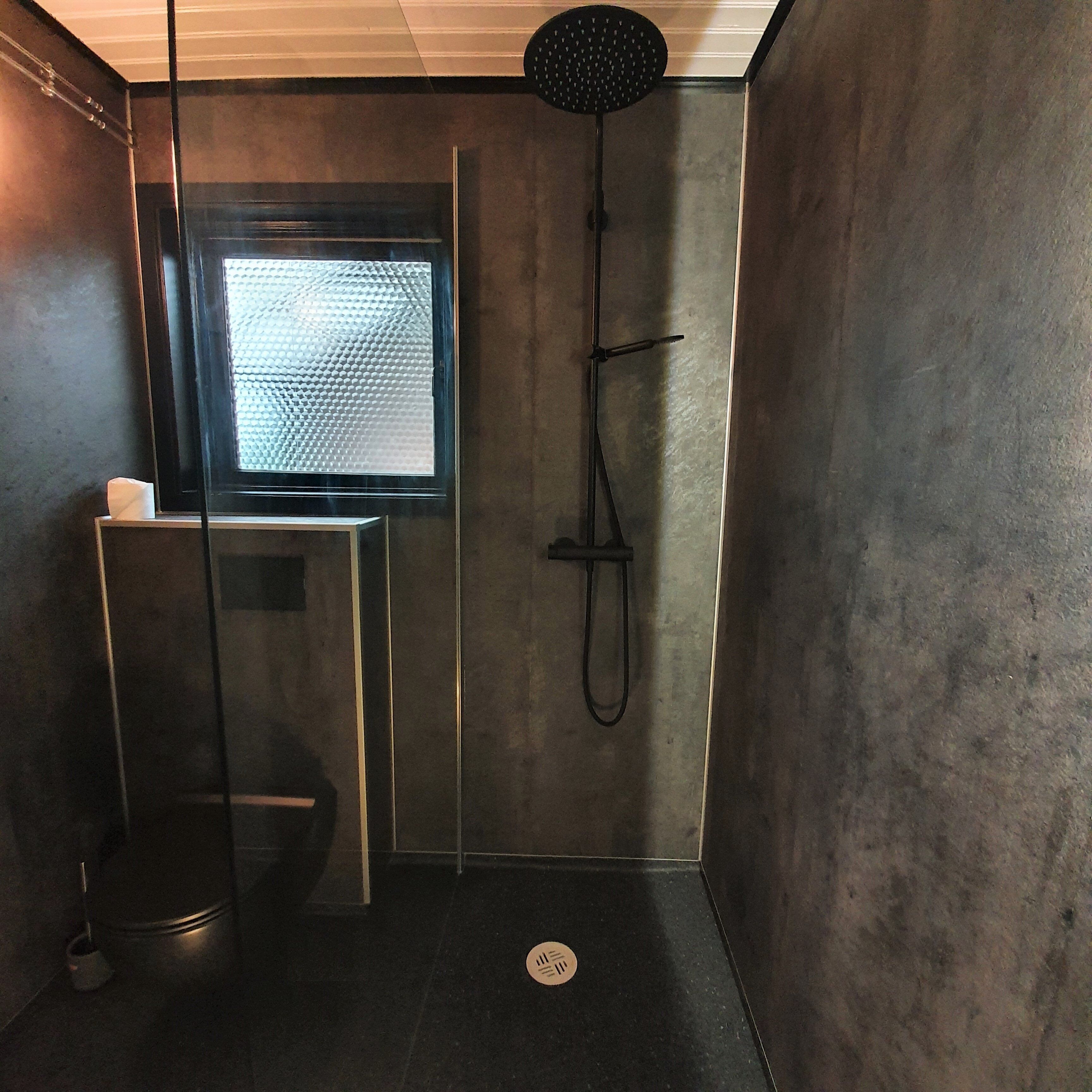 A bathroom with a shower, a toilet, and a window.