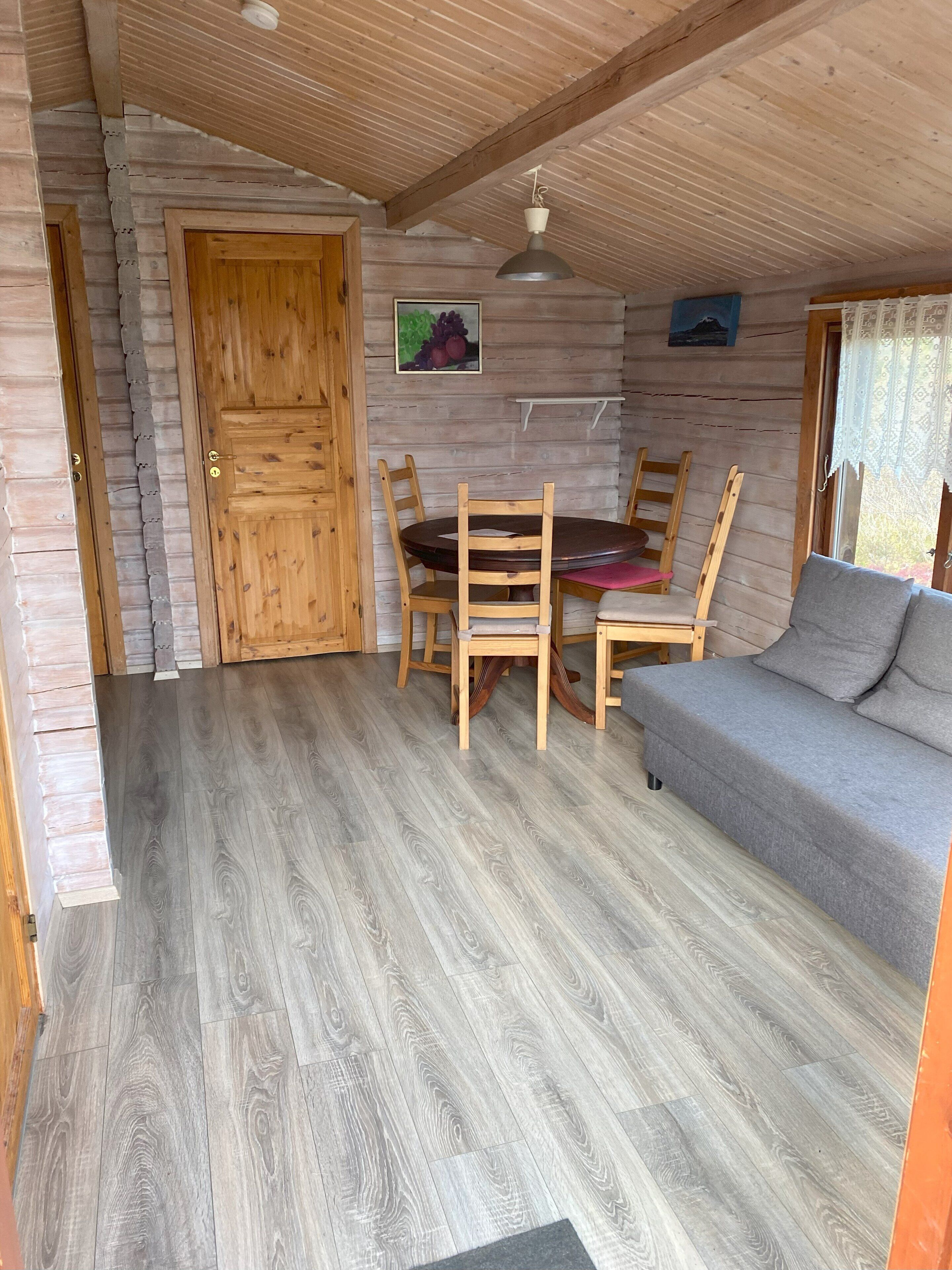 A cozy room with a wooden door, a dining table with chairs, and a grey sofa.