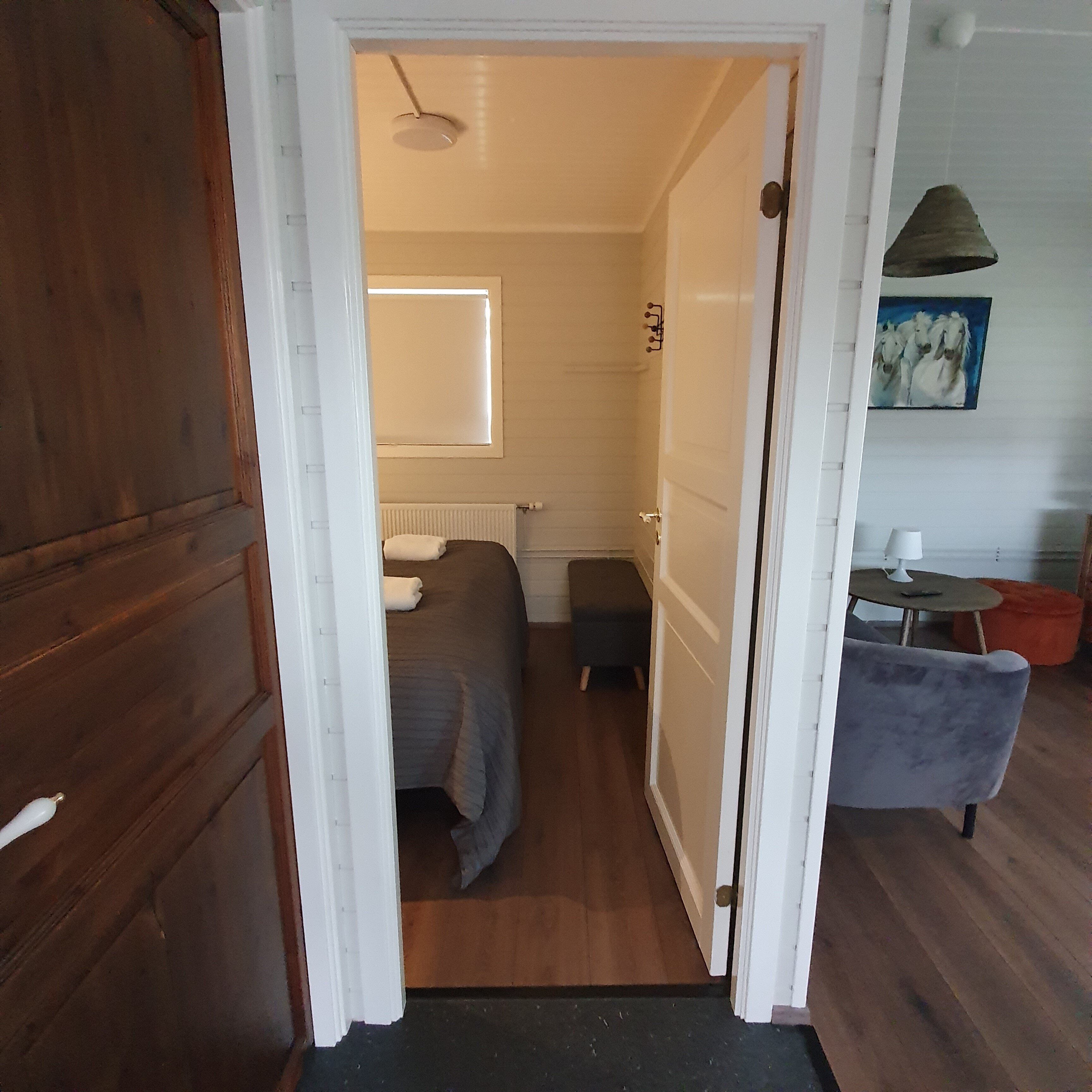 A narrow doorway leading into a room with a bed, a radiator, and a small stool.