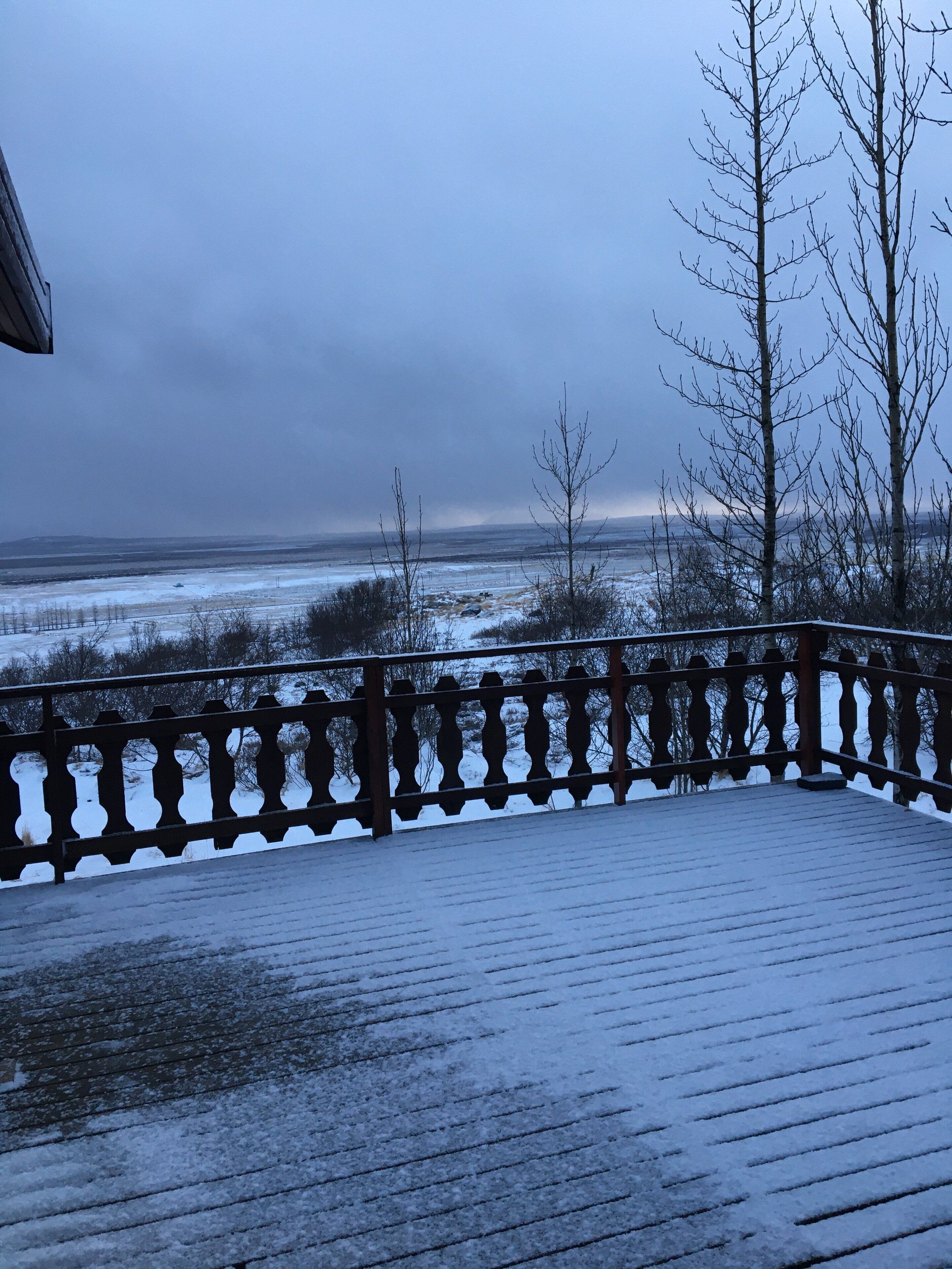 Um deck de madeira com guarda-corpo, com vista para uma paisagem coberta de neve.