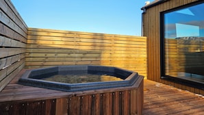 Una terraza de madera con un jacuzzi y un ventanal grande.