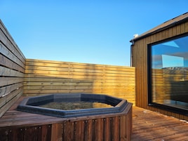 Una terraza de madera con un jacuzzi y un ventanal grande.